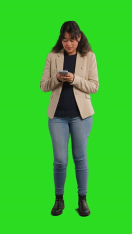 tomada de estudio de video vertical de una mujer de negocios usando un teléfono móvil para enviar mensajes o navegar en línea de pie contra la pantalla verde 2