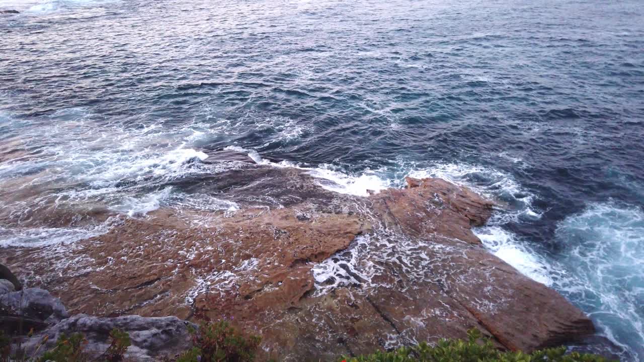 Ombak laut memercik di pantai berbatu Pantai Bondi di Sydney, Australia saat matahari terbenam