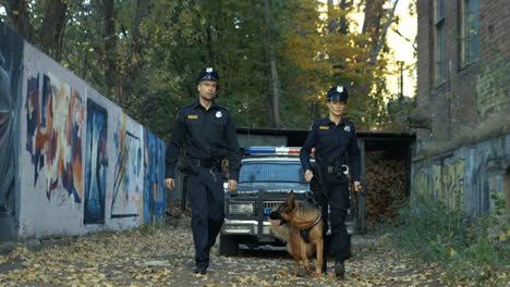 Policía-Y-Mujer-Policía-En-Uniformes-Caminando-Con-Perro-Pastor