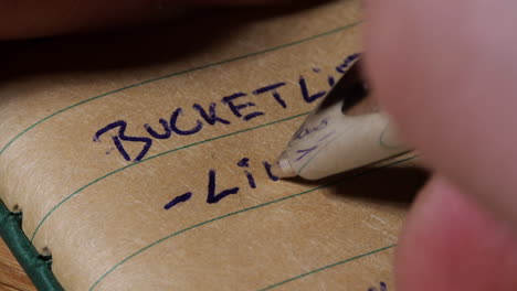 person writing self help bucket list goal setting to live aim on brown lined paper journal, close up