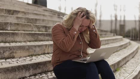 bionda stanca con mal di testa che scrive sul portatile