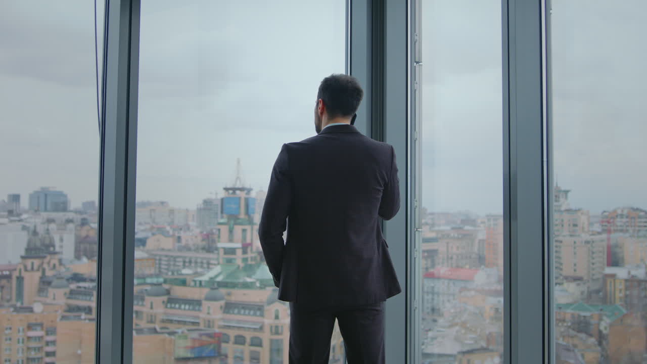 gerente de la compañía llamando a los socios mirando por la ventana de la oficina. hombre hablando por teléfono