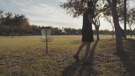 man throws a disc golf frisbee with a backhand throw next to a disc golf basket