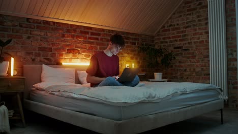 Young man working on laptop in a bedroom at night