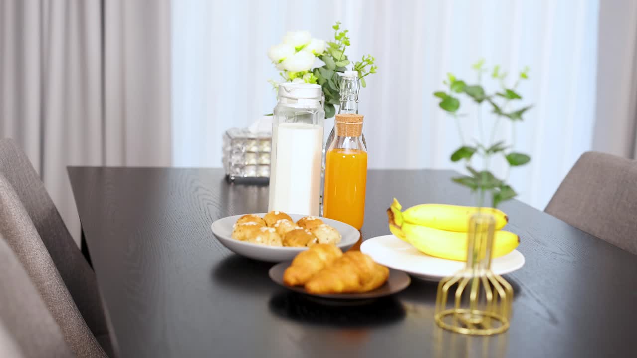 Bananas, croissants, milk, and juice arranged on a table in bright, natural morning light
