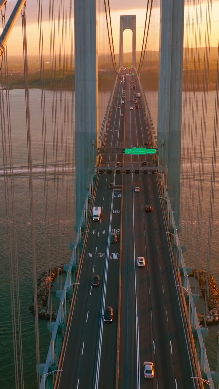 New York Whitestone bridge with cars moving along. Sunset over the river and boat sailing under the bridge. Vertical video