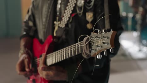 a guitarist close up during the performance on the set ready to start playing, the guitarist color is red and the guitarist wore a black rock star jacket, other band is in the background