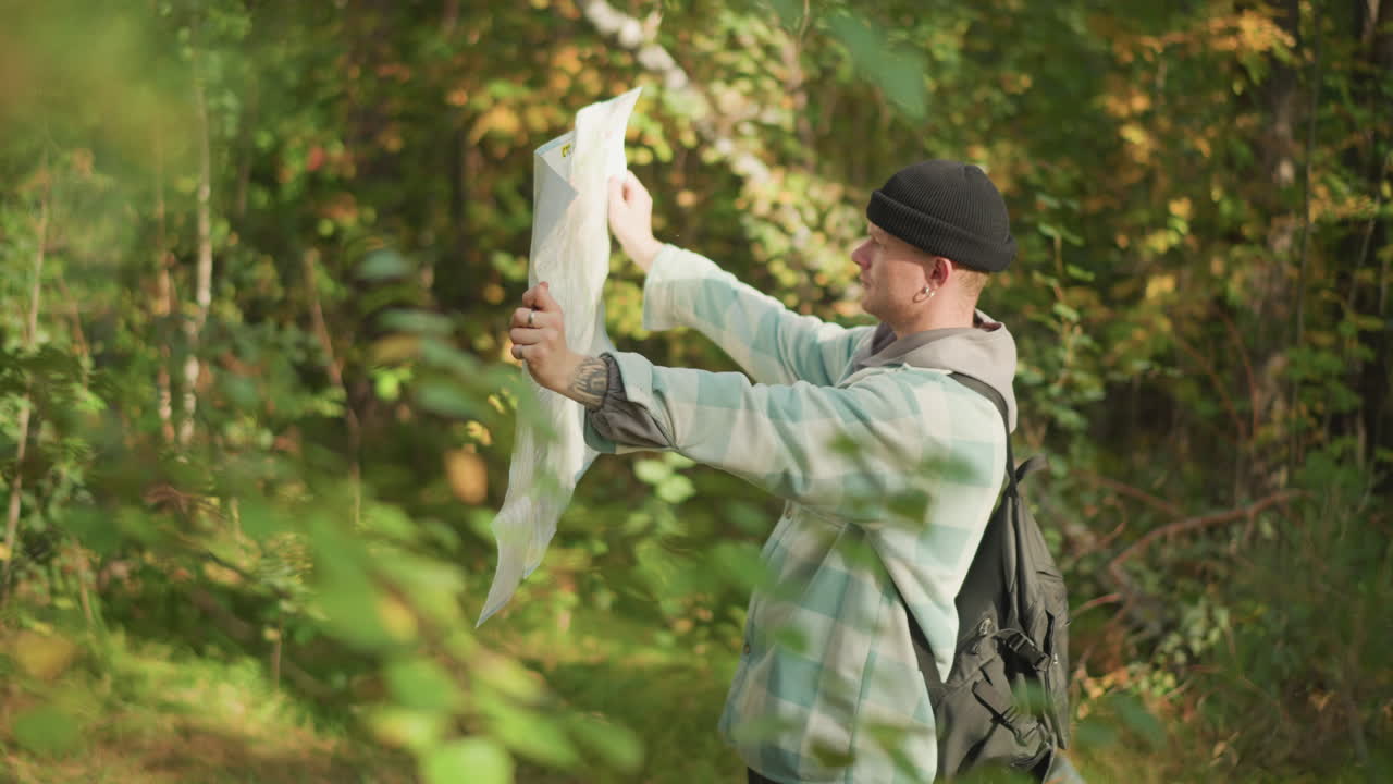 White male backpacker holding map aloft in leafy forest, relieved navigator celebrating found route, joyful moment with sunlight through canopy, decisive outdoor explorer finishing orientation