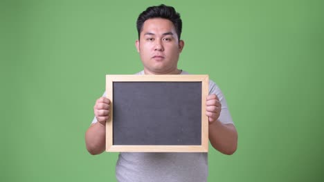 young handsome overweight asian man against green background