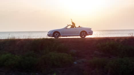 woman driving a convertible car at sunset on the beach