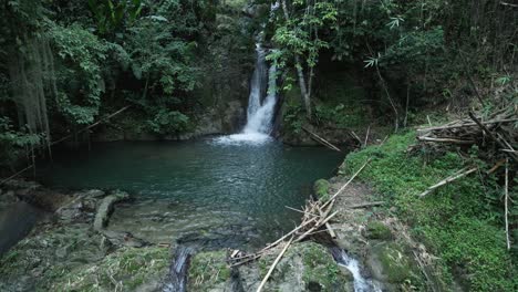 Amazing-aerial-view-of-a-cascading-waterfall-in-slow-motion-with-a-young-woman-standing-at-the-base