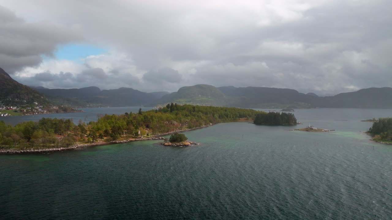 Ilhas costeiras e águas calmas do fiorde rodeando uma ilha com a cidade de Jorpeland ao fundo, Noruega Ocidental, vista aérea.