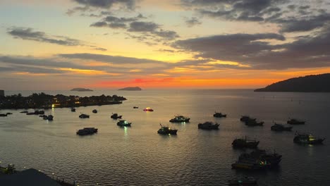 aerial panoramic view of kota kinabalu waterfront dock at sunset, view of many moored fishing boats by the coast in silhouette, and isles in backdrop