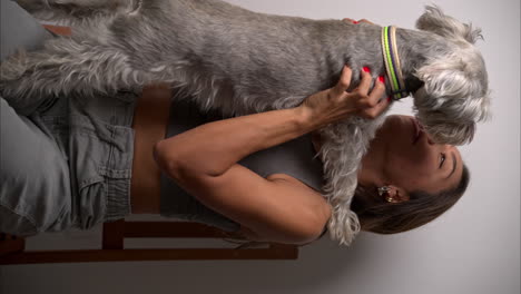 vertical slow motion of brunette hispanic female model petting her schnauzer dog on her lap and hugging it