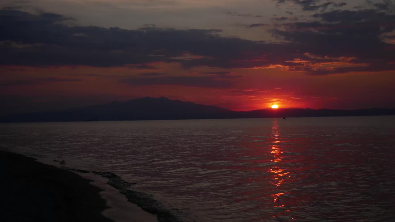 таймлапс заката на пляже тасос, греция, с неопознанными людьми, проходящими мимо, и летающим вокруг дроном