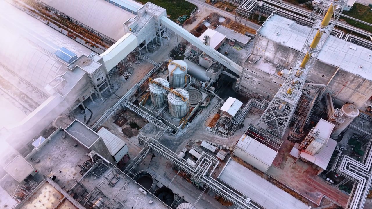 Intricate piping and tanks at a factory. An overhead aerial view displays a complex network of industrial pipes and metallic storage cylinders.