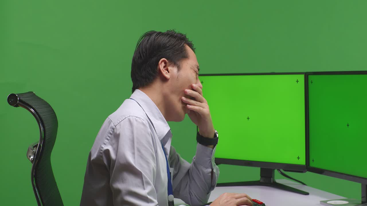 녹색 스크린 스튜디오에서 모의 여러 컴퓨터 모니터와 함께 작업하는 동안 잠자리에 들기 전에 는 피곤한 아시아 남자의 근접