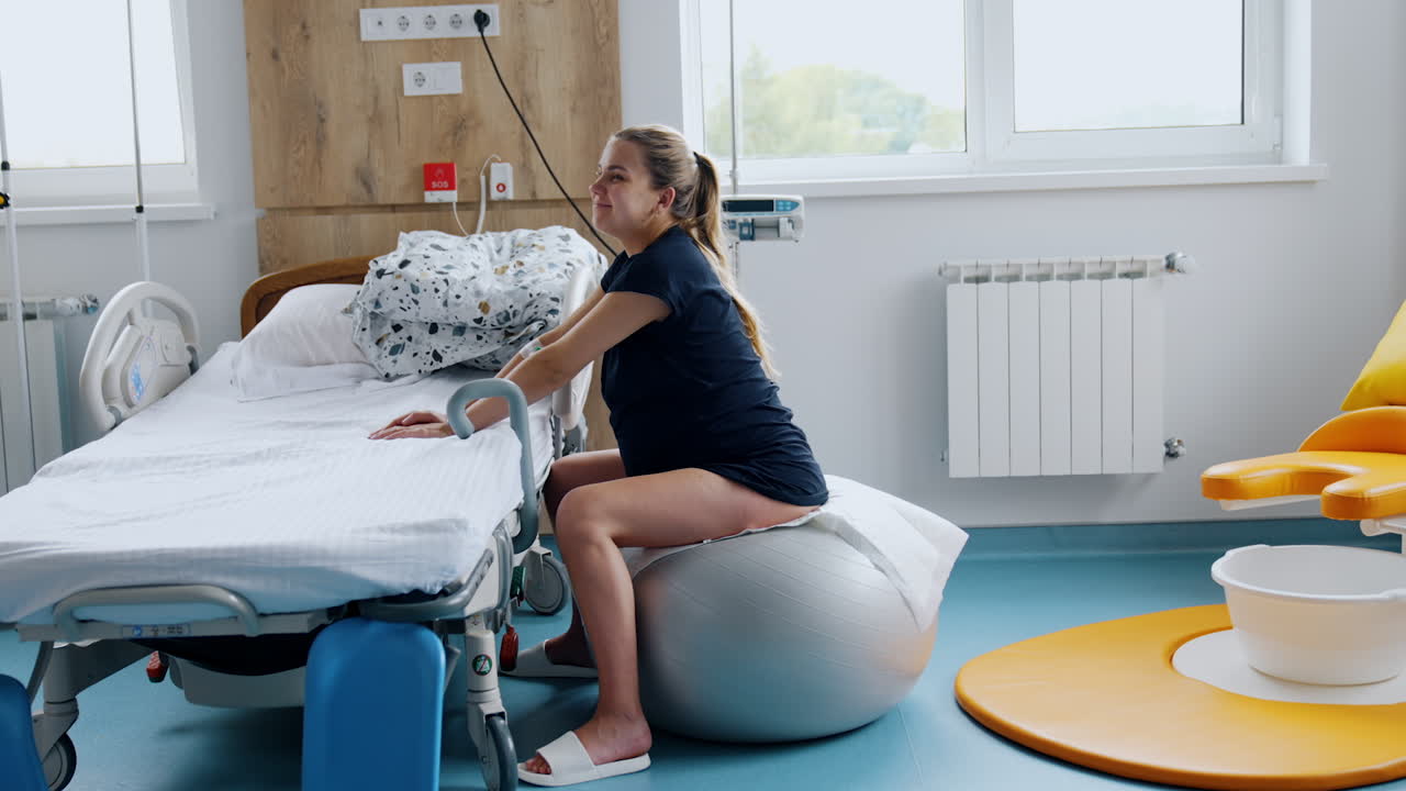 Pregnant woman sitting on the fitball during contractions. Lady moves back and forth to relief pain.