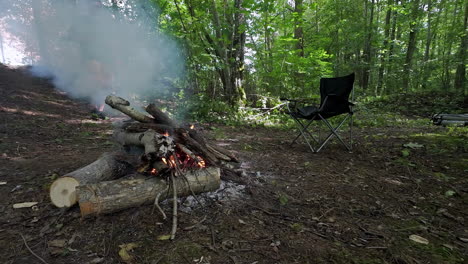 male walking with a drink in his hand towards unfolded camping chair near a campfire