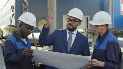 engineer talking to plant workers outdoors and showing blueprint