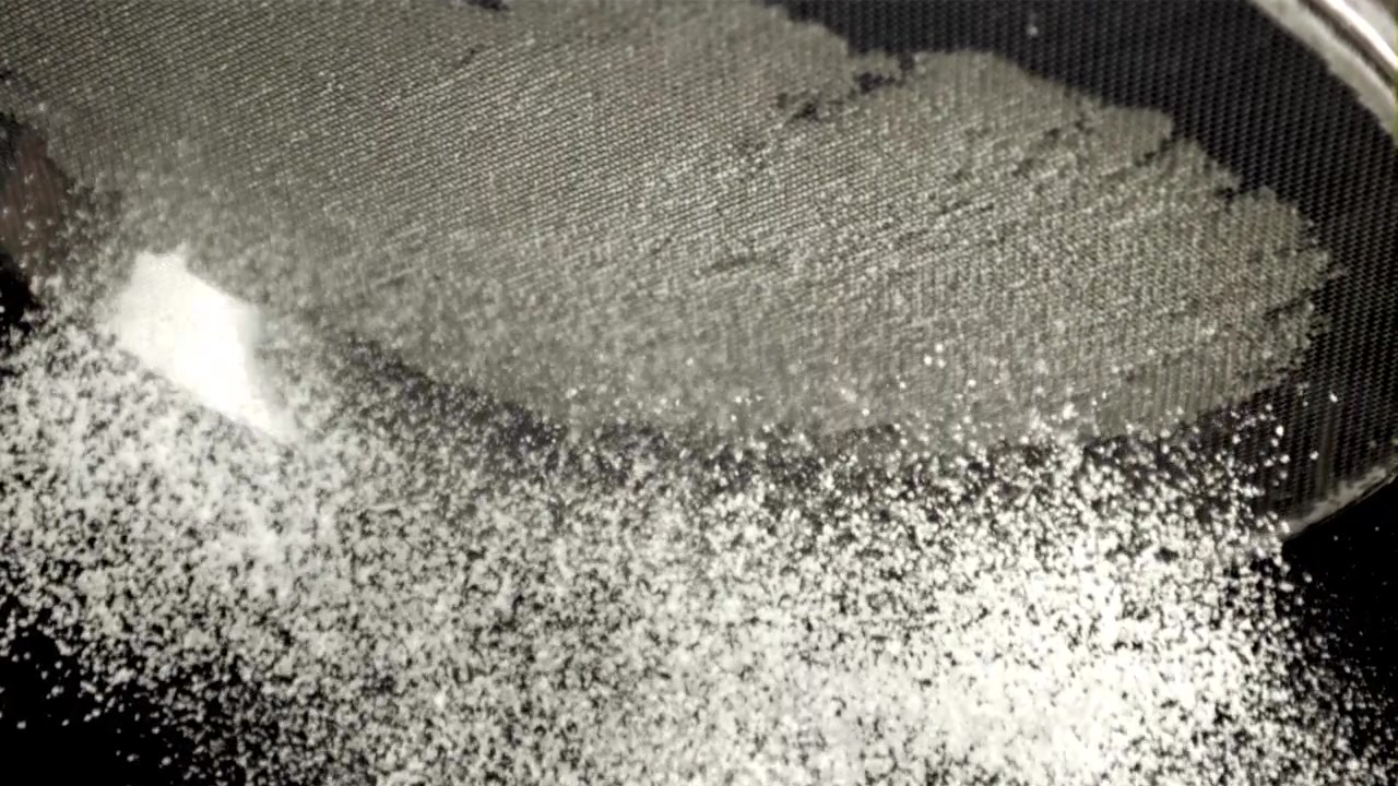 Slow Motion Sifting of White Powder Through a Fine Mesh Sieve