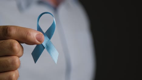 close up of man holding blue ribbon badge symbolizing awareness of men's health and cancer