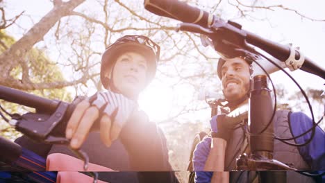 pareja de ciclismo de montaña llevando una bicicleta e interactuando entre sí