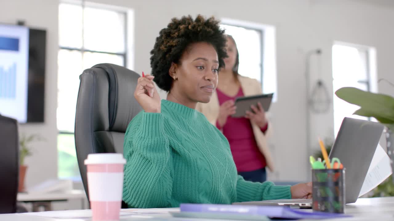 Diverse business female colleagues in discussion using laptop in casual office meeting, slow motion