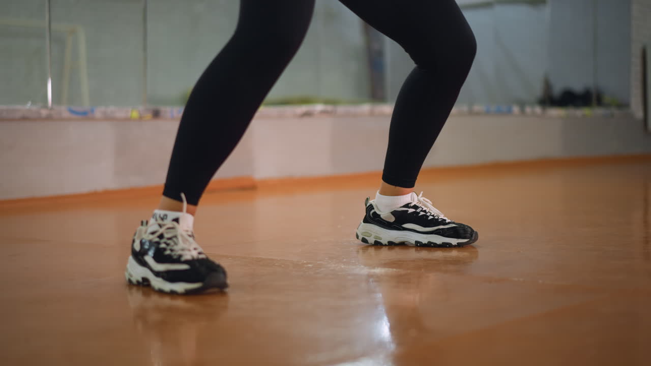 Close view of legs in black leggings and sneakers moving on polished wooden floor inside fitness studio, capturing focus, rhythm, and dynamic energy of active workout with balance and control
