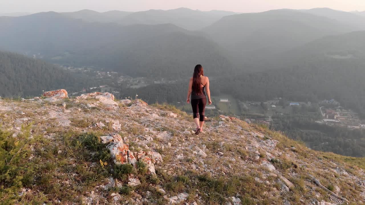 una joven se acerca al borde de la roca y levanta las manos con alegría.