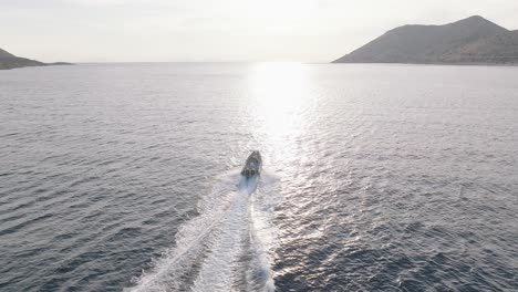 aerial orbiting shot of motorboat speeding on mediterranean sea against golden sunlight at sunset in greece, cinematic