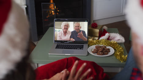 Rückansicht-Eines-Kaukasischen-Paares-Mit-Weihnachtsmützen,-Das-Während-Der-Weihnachtszeit-Einen-Videoanruf-Auf-Dem-Laptop-Führt