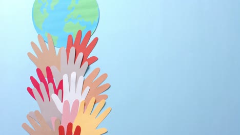 close up of hands together with globe made of colourful paper on blue background with copy space