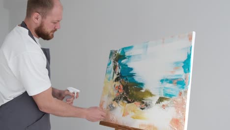 artist working on an abstract painting with a sprayer and brush