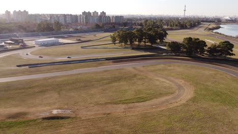 aerial view of autodromo racetrack with driving race cars on asphalt road during sunny day - skyline of buenos aires in background