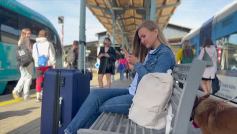 slow motion sequence of young blonde woman waiting for her train at railway station, checking her smartphone and looking at arriving train. blonde watching incoming train approaching. slow motion