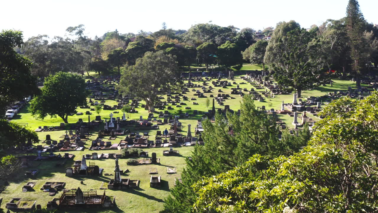 Dron aéreo volando lentamente entre árboles para revelar un gran cementerio en un día soleado en Australia.