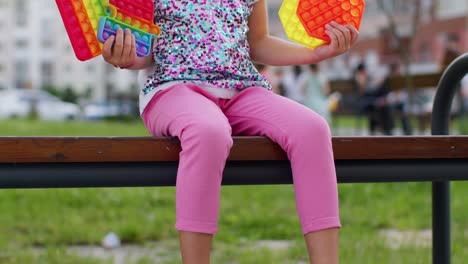 stylish children girl squeezing presses anti-stress push pop it popular toy on playground bench