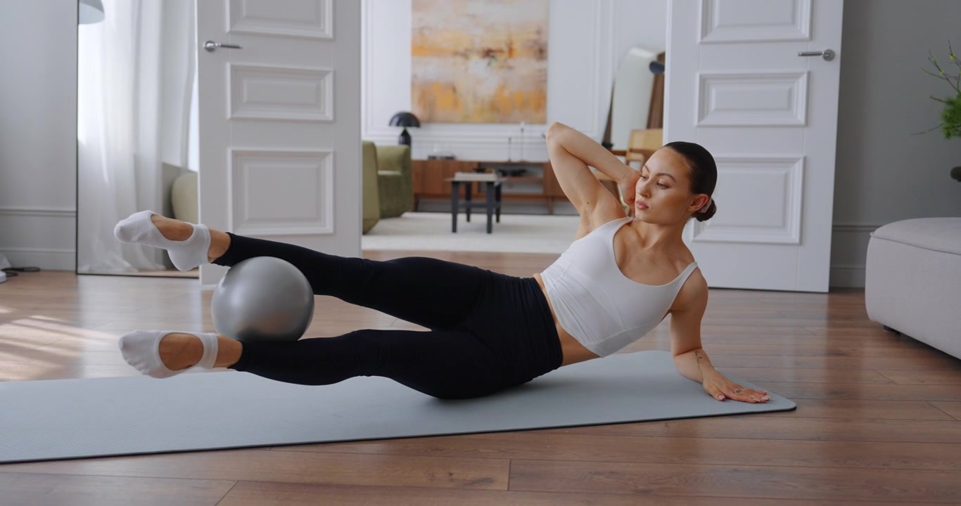 Young Woman Performing Pilates Side Leg Lifts with Ball at Home