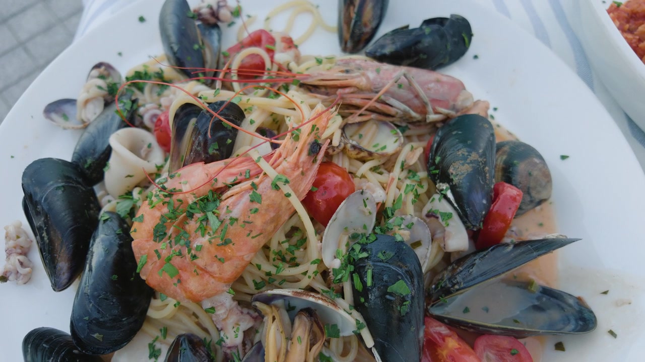 Close-up of a seafood pasta with mussels, clams, shrimp and cherry tomatoes on a white plate