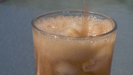 pouring a refreshing fizzy drink over ice outside on a sunny day