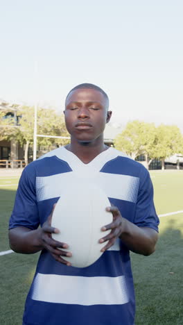 vertical video: rugby player holding ball on field, focusing with eyes closed, preparing for game