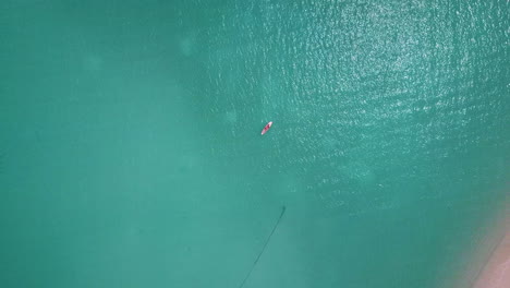 Tiro-De-Dron-En-Aumento-De-Un-Hombre-Tendido-En-Una-Tabla-De-Surf-O-En-Una-Tabla-De-Remo-En-El-Océano