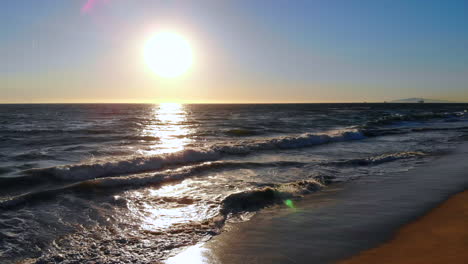 Perfect-pull-back-from-beautiful-ocean-sunset,-over-waves,-seagull-flies-by,-to-reveal-wide-empty-Huntington-Beach-in-Southern-California-with-4k-aerial-drone