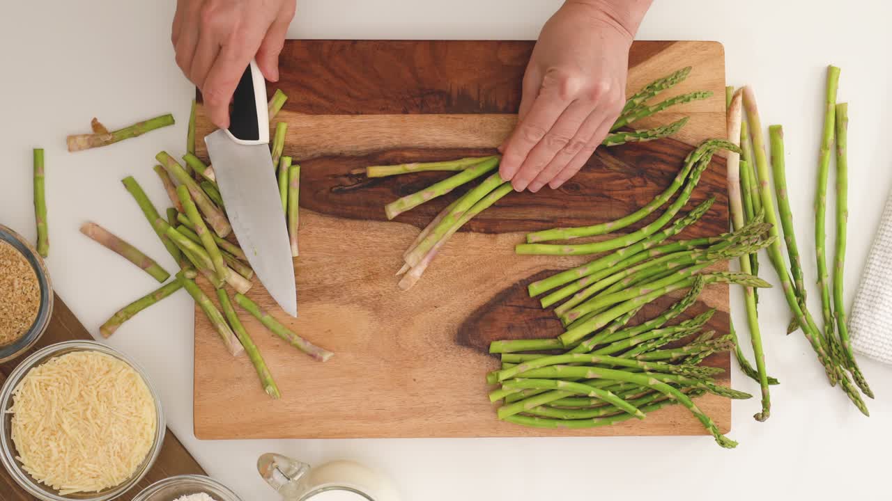 Woman hands cutting fresh green asparagus on wooden cutting board, loop