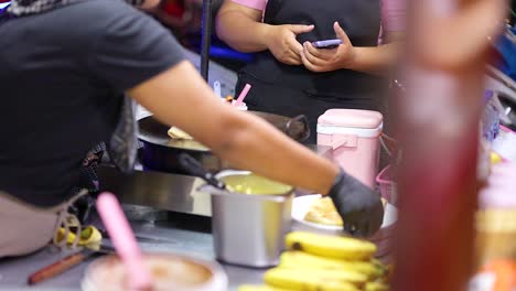a street vendor prepares roti at a bustling night market in phuket, thailand. the scene captures vibrant colors and dynamic movement