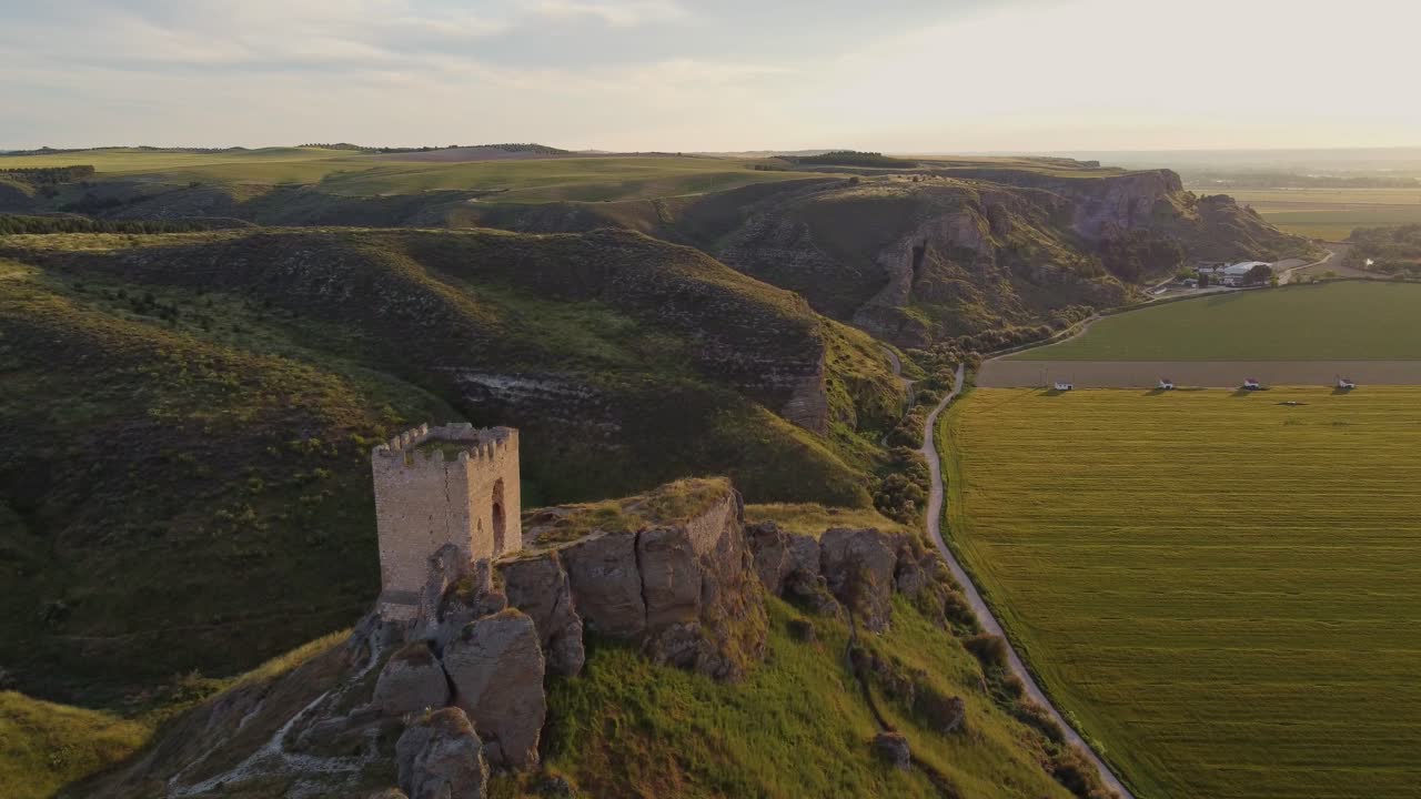 Drone shot of the medieval Oreja Castle perched on a hilltop at golden hour near Aranjuez, Spain. Scenic sunset over rural fields and rocky landscape.