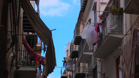 a man hangs clothing from his balcony across from other apartment buildings in cefalu italy