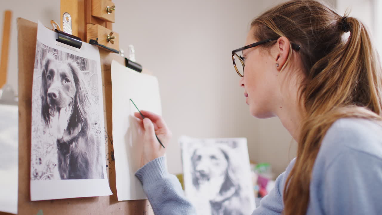 십대 여성 예술가 가 석탄 에 있는 사진 에서 개 의 그림 을 그리는 좌석 에 앉아 있다
