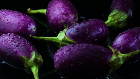 Toma-En-Cámara-Lenta-De-Berenjenas-Moradas-Salpicadas-De-Agua-En-Una-Superficie-Negra